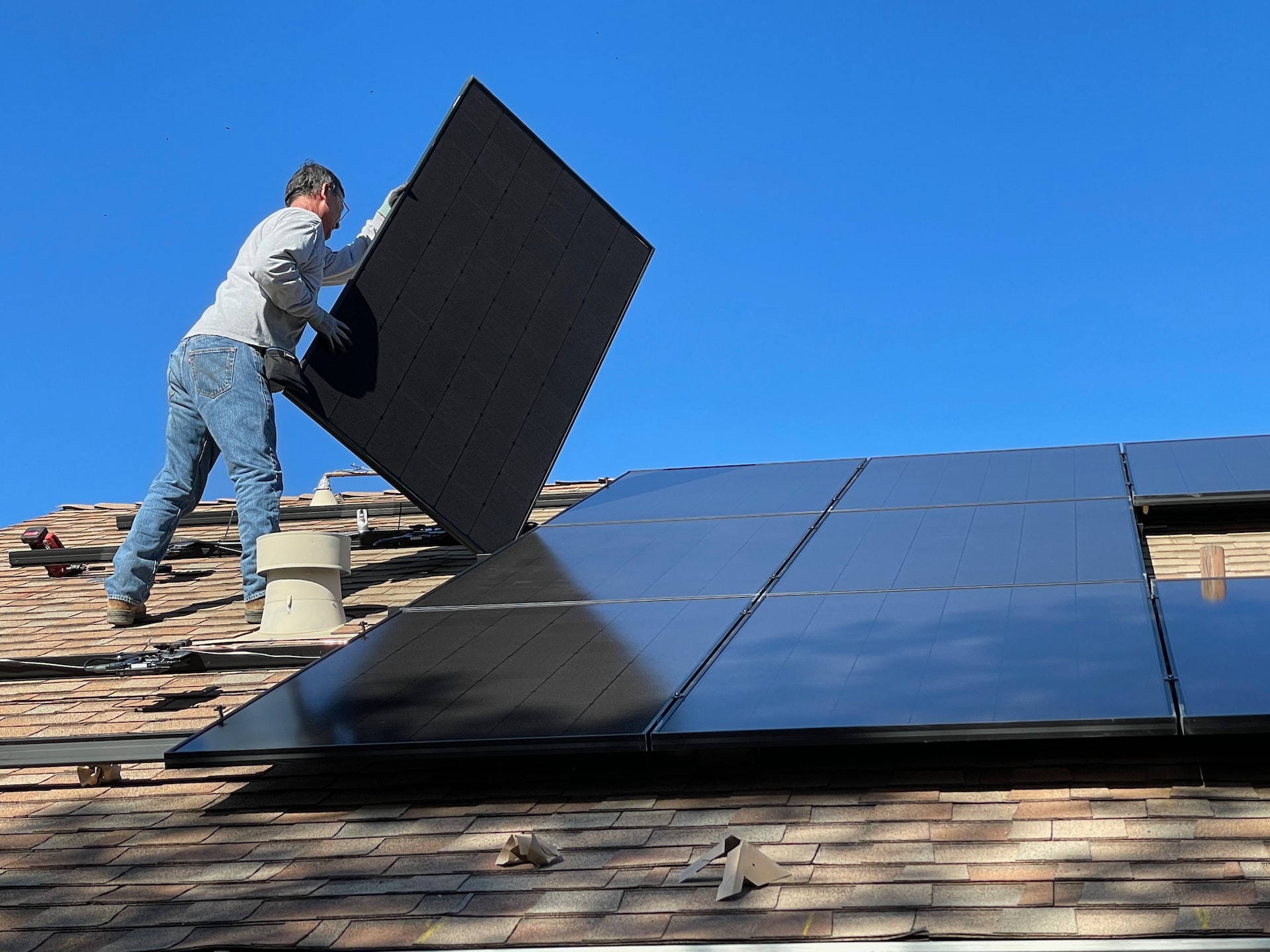 Męzczyzna montuje panele fotowoltaiczne na dachu domu